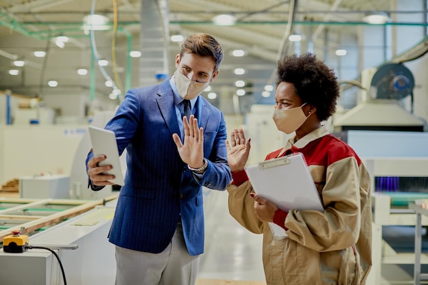 Happy company manager and female worker waving during video call at woodworking production facility