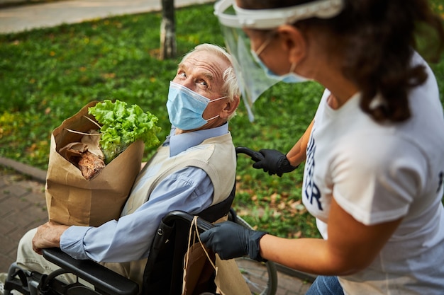 Happy confident male in blue shirt in wheelchair spending time with woman volunteer