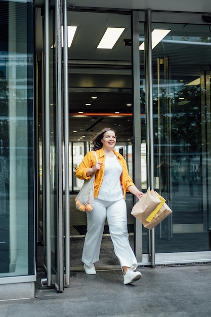 Happy confident smiling plus size curvy young woman with shopping bags walking on city street near shop windows