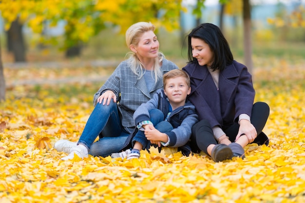 A happy, content same sex female couple and their son in a happy family theme with yellow fall leaves.