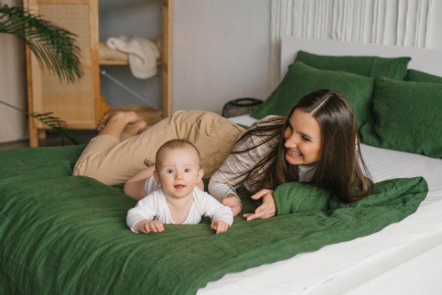 Happy and contented mother is resting on the bed with her baby son Motherhood