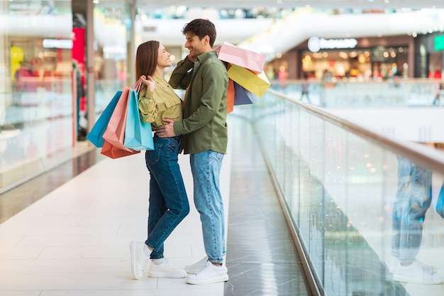 Happy couple of buyers shopping together standing embracing in mall