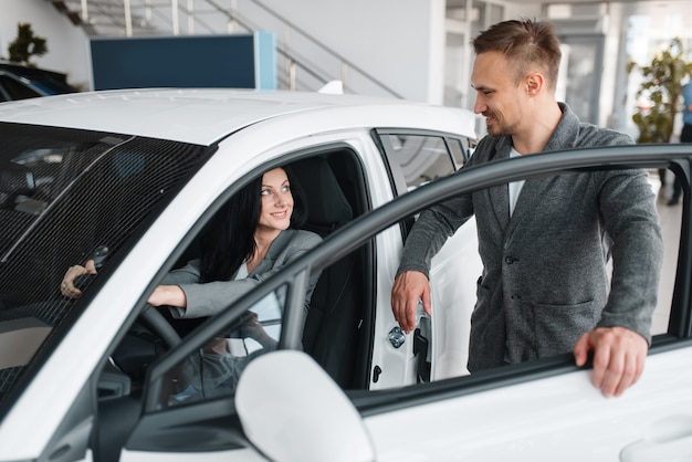 Happy couple buying new car in showroom, woman behind the wheel.