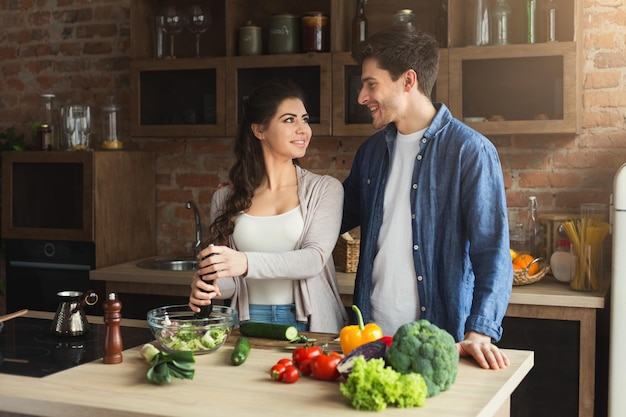 Happy couple cooking healthy food together in their loft kitchen at home. Preparing vegetable salad, copy space