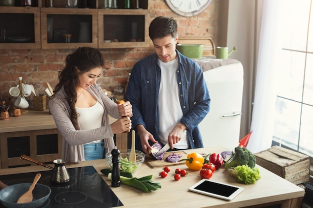 Happy couple cooking healthy food together in their loft kitchen at home. Preparing vegetable salad, copy space