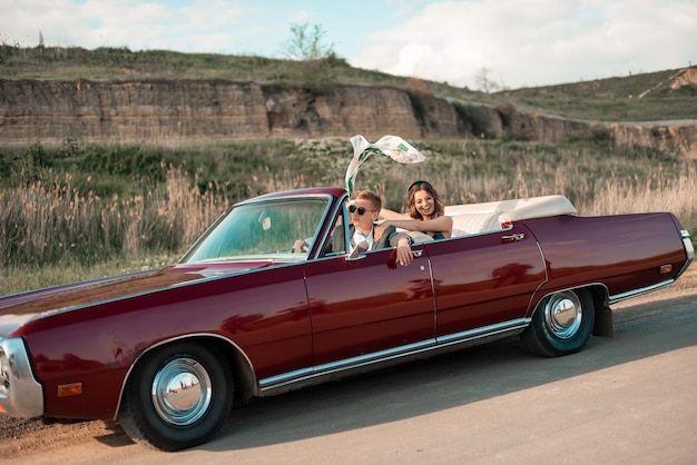 Happy couple driving down country road into sunset in vintage cabriolet car