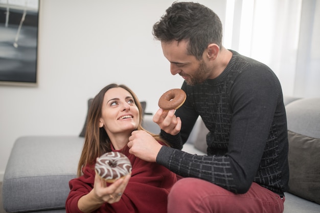 Happy couple eating donuts at home