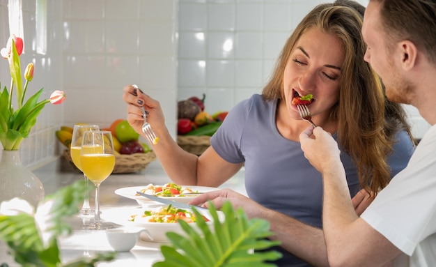 Happy couple eating salad in kitchen at home Young man giving strawberry to his girlfriend