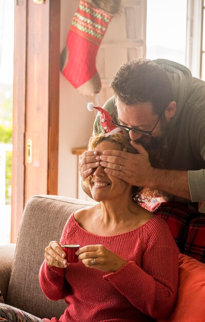 Happy couple enjoy christmas holiday celebration at home with happiness Man closing eyes to his woman to give her a xmas present gift Surprise from behind concept Traditional gift sharing leisure