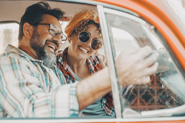 Happy couple having fun inside a car during travel adventure Cheerful man and woman smiling and laughing a lot together People enjoying vehicle trip in friendship and relationship Concept of drive