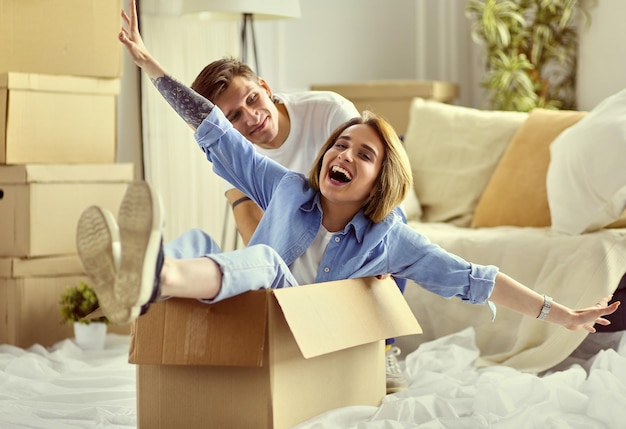 Happy couple having fun and riding in cardboard boxes at new home