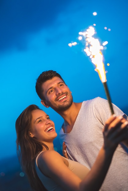 The happy couple hold a firework stick. evening night time