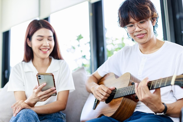 Happy couple at home A Young man playing guitar to girlfriend in living room Leisure activities