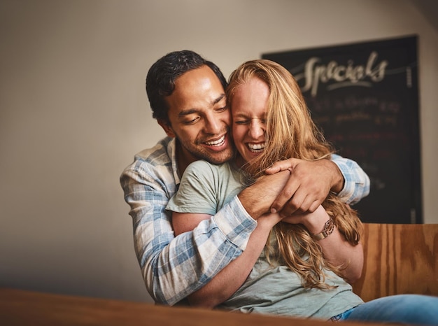 Happy couple hug and smile for romance embrace or relationship happiness at indoor restaurant Young man hugging woman and smiling for fun love or dinner date spending bonding time at cafe together