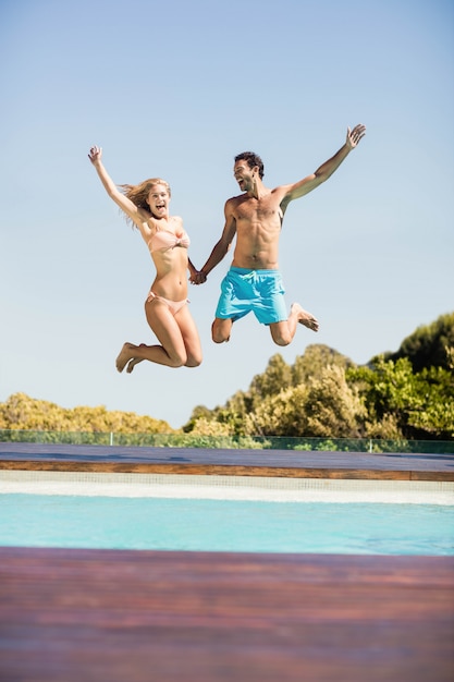 Happy couple jumping in the pool in a sunny day