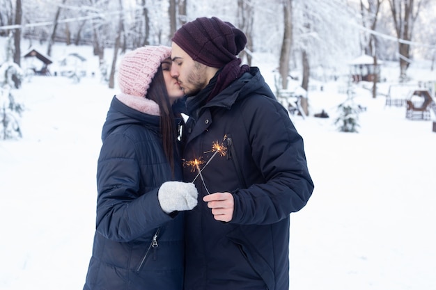 Happy couple kissing and holding sparkles in park with snow