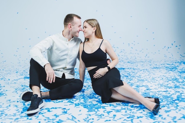 Happy couple laughing at gender party while sitting in blue confetti Gender party