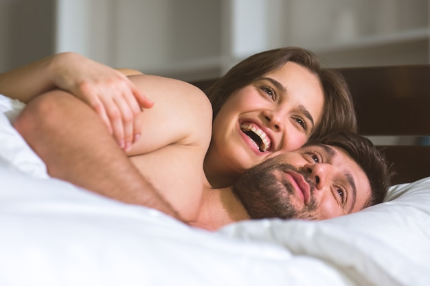 The happy couple lay in the white linens on the bed