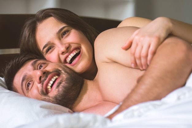 The happy couple lay in the white linens on the bed