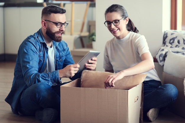 Happy couple looking at photo album while unpacking stuff after relocation to new flat