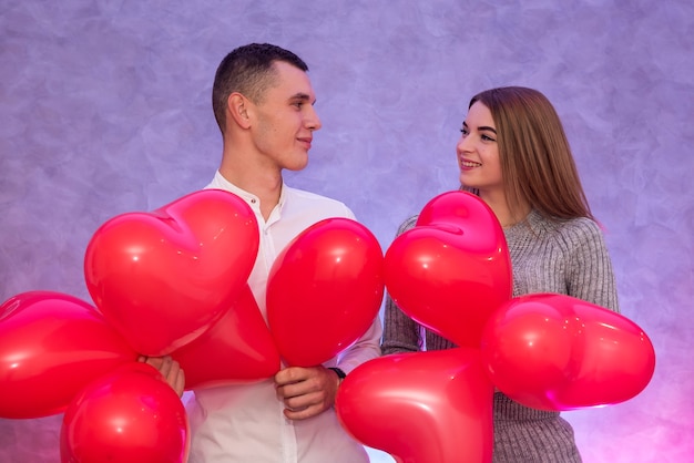 Happy couple in love posing with red air balloons in shape of heart