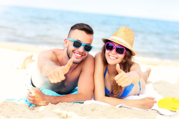 happy couple lying on the beach and showing ok signs