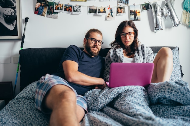 Happy couple lying in bed indoor looking at computer