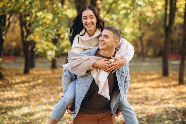 Happy couple man holding a woman behind his back and having fun together in the autumn park