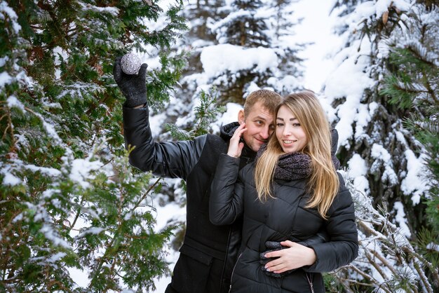 Happy couple of men and women outdoors decorates christmas tree outdoors in warm clothes in snowy pa...