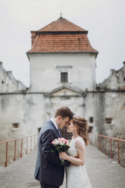 Happy couple of newlyweds posing near castle fairytale wedding moment beautiful bride and groom hug near ancient castle entrance in Europe