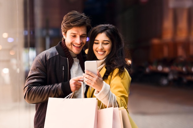 Happy couple ordering taxi on cellphone walking near city center