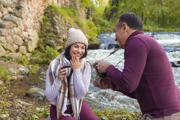 A happy couple on a picnic by the river is photographed for memory.