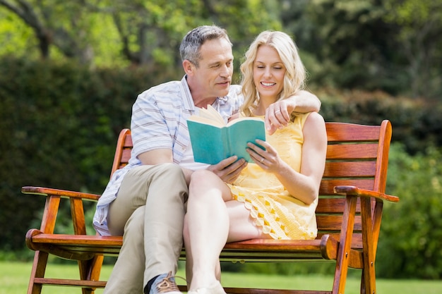 Happy couple reading a book on the bench outside