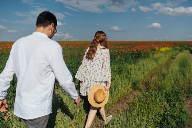 Happy couple running and flirting between the grass on a green poppy field in spring