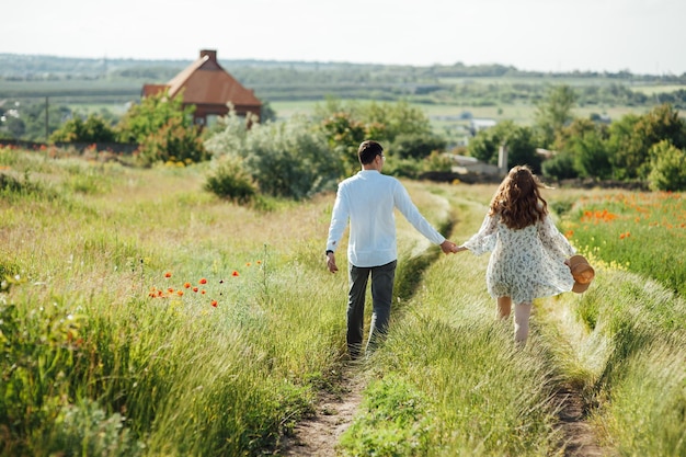 Happy couple running and flirting between the grass on a green poppy field in spring