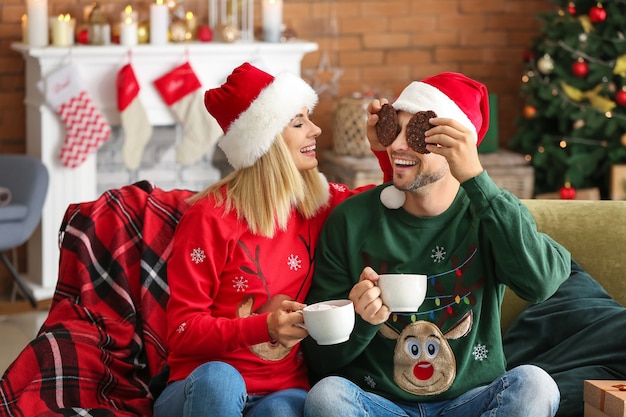 Happy couple in Santa hats drinking hot chocolate and eating cookies at home