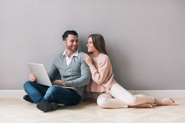 Happy couple shopping online on laptop while sitting floor at home.