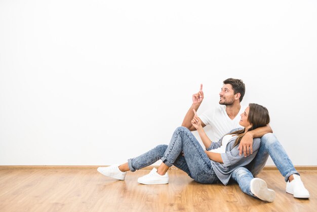 The happy couple sit and gesture on the background of the white wall