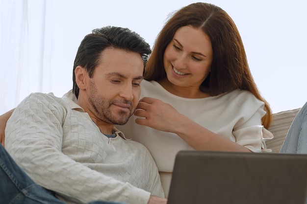 Happy couple sitting on the couch in her arms looking at laptop