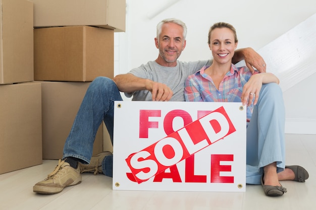 Happy couple sitting on floor with sold sign