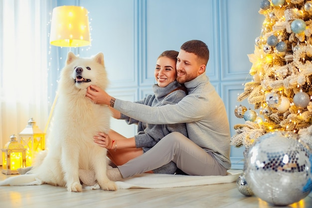 Happy couple sitting and hugging near Christmas tree at home hearth home clothes and sweaters