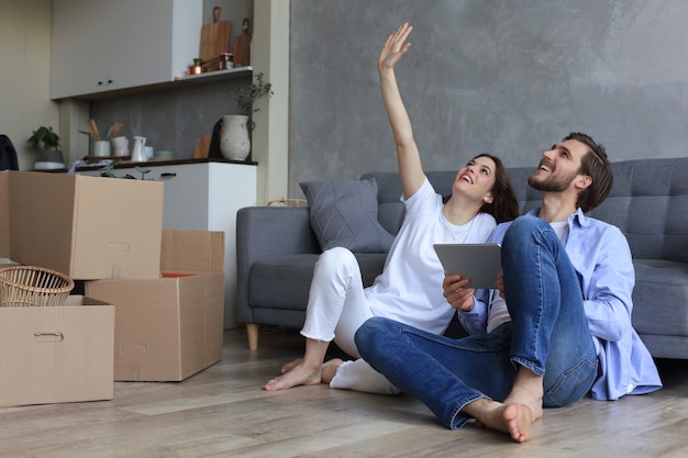 Happy couple sitting and planning new home decoration at home with a tablet at moving day, renovation and interior design for new house.