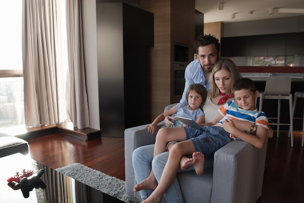 happy couple spending time with kids using tablet computer on an armchair at home