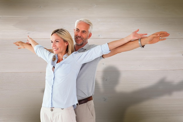 Happy couple standing with arms outstretched against bleached wooden planks background