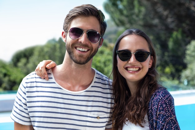 Happy couple in sunglasses standing near the pool