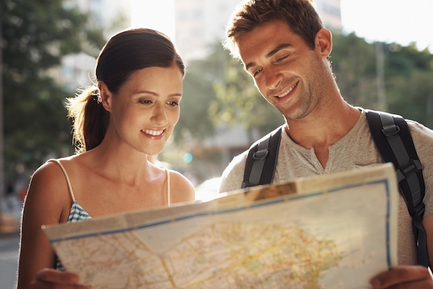 Happy couple tourism and city with map for destination location or tour guide on street or road Man and woman looking at paper with smile for directions travel route or outdoor path in urban town