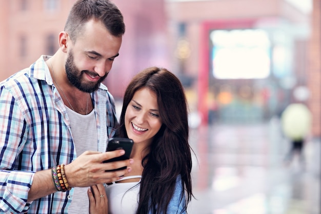 Happy couple of tourists using smartphone in city in rainy day