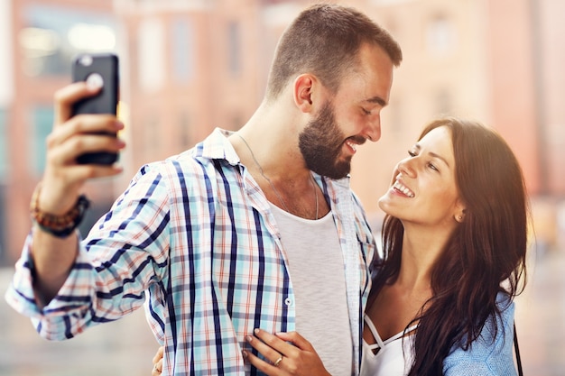 Happy couple of tourists using smartphone in city in rainy day