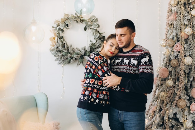 Happy couple in traditional sweater decorating Christmas tree together at home