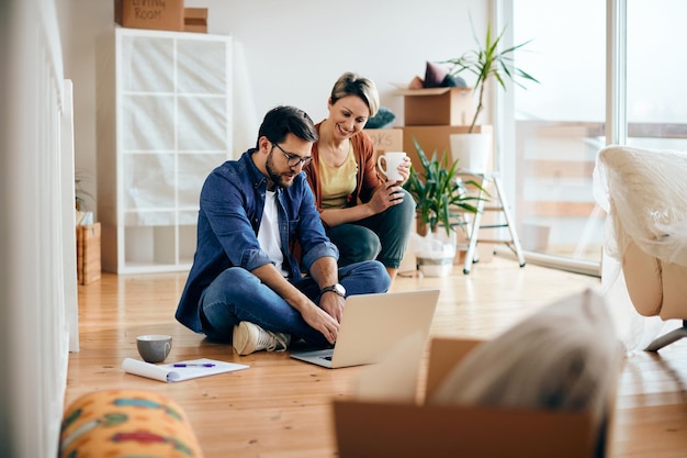 Happy couple using laptop while moving into a new apartment